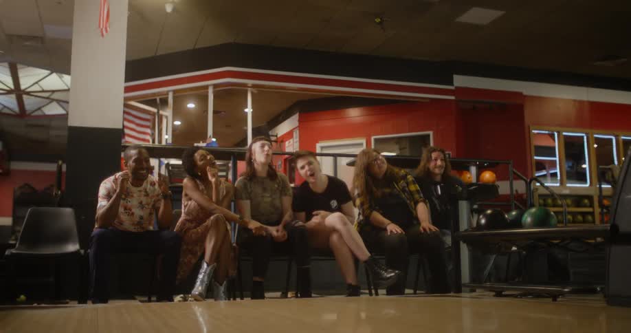 Friends sitting watching a person throwing a bowling ball