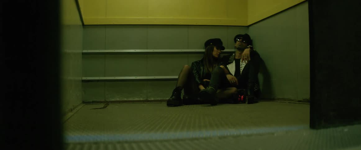 A man and a woman in black clothes are sitting on the floor leaning against a wall