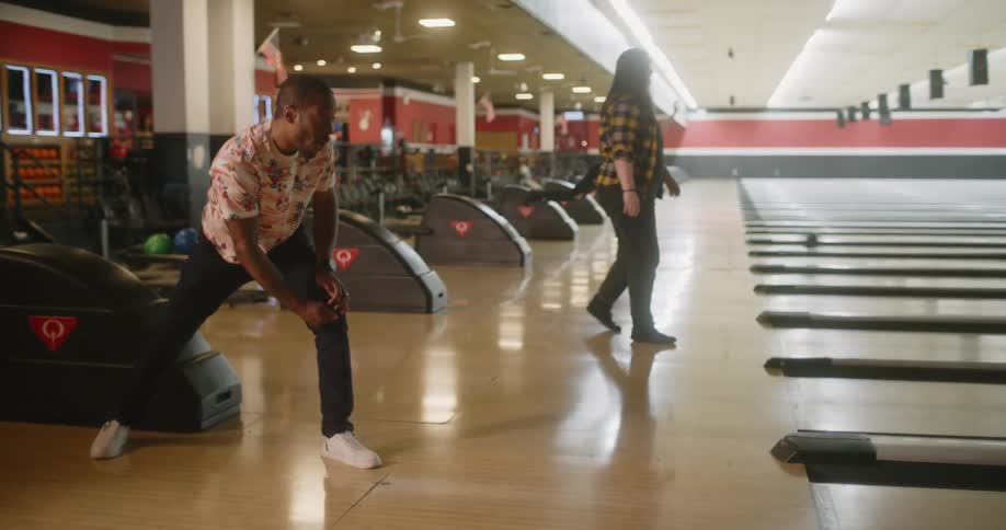 A man throwing a bowling ball on a wooden court and he celebrates afterwards
