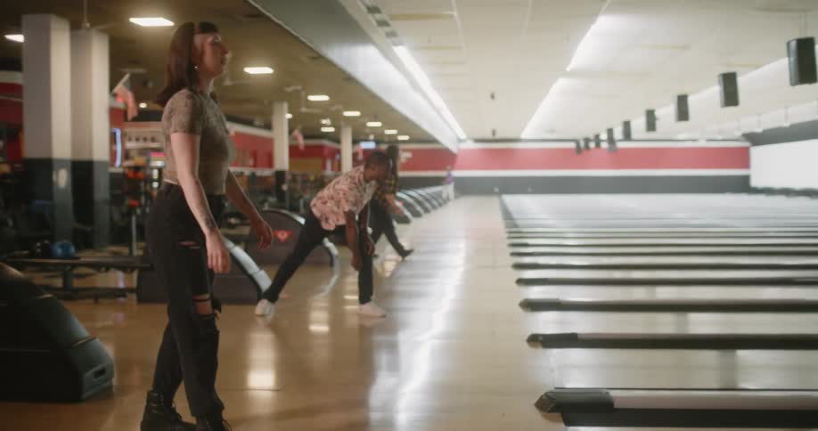 A woman in a bowling alley has a green ball and throws it into the lane