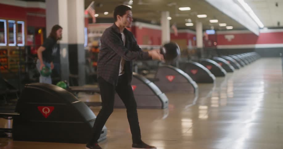Two bowlers bowl down adjacent lanes and one gets a good result as their friends watch