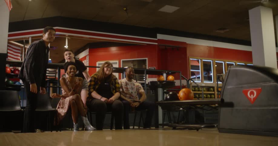 Some people sitting happily talking and a person in front of them is judging a green bunk ball on a wooden floor
