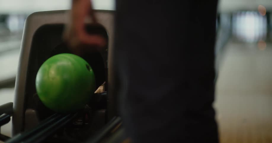 A man waits for a machine to return his bowling ball then picks it up when it comes out