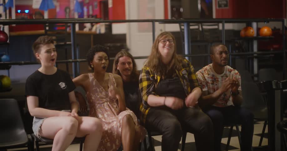 Friends cheer and groan while bowling at a bowling alley