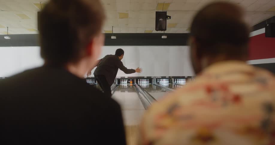 Friends sitting and watching their colleague throw a ball in a bowling game