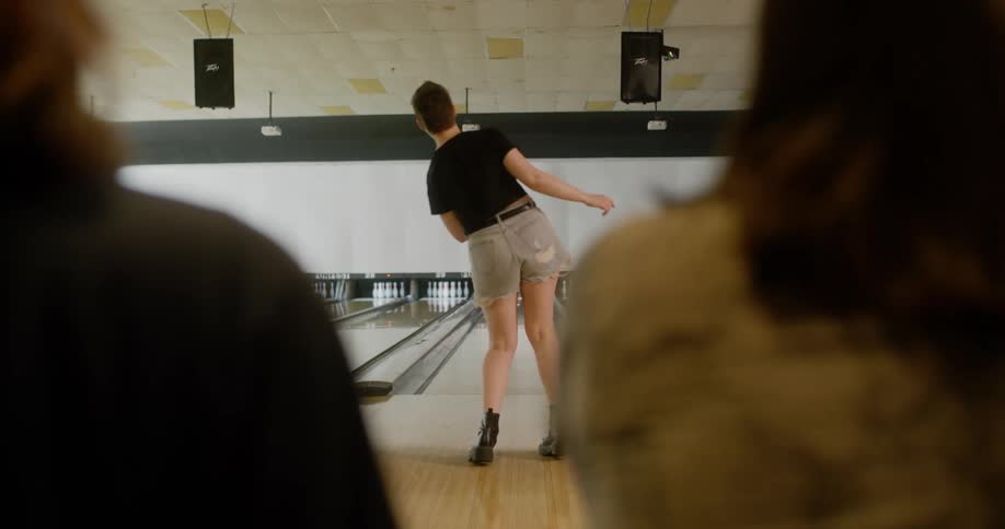 Friends sitting smiling watching their colleague throw a ball in a bowling game