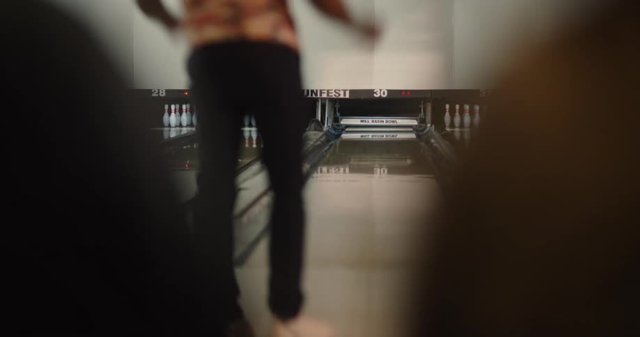 Person throwing a ball in a bowling game and his friends cheering