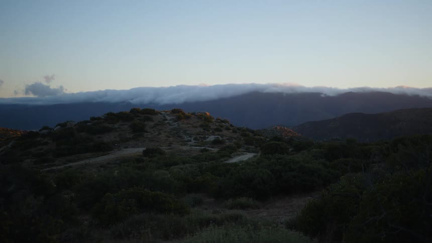 Low clouds passing above mountains as the day fades to dusk