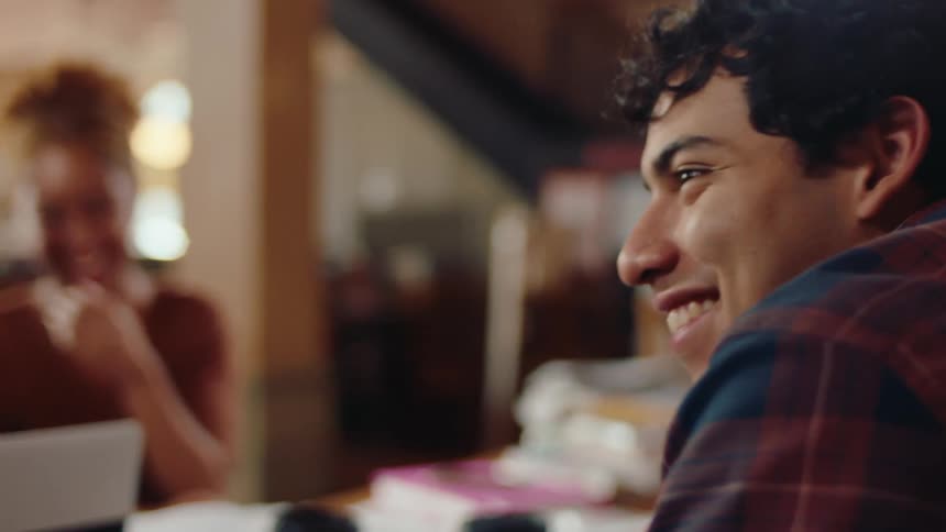 Three people are sitting at a table and are happy and two of them are using a laptop and talking