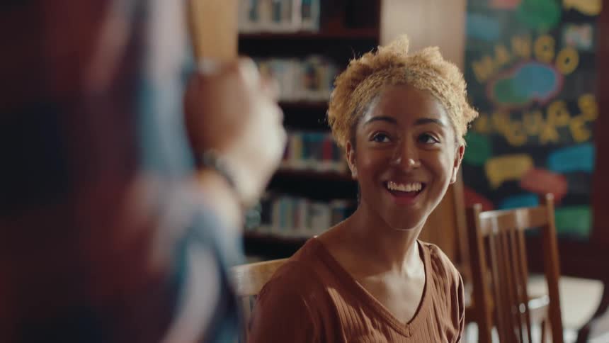 Teenage girl laughs with a friend in the library