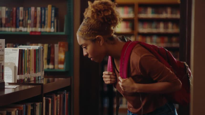 Woman walking through a library and picking up a book