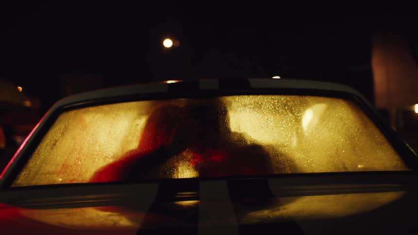 Couple is silhouetted against the windshield while kissing in a parked car at night