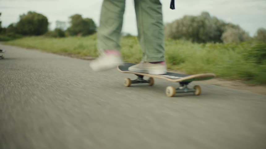 Two skateboarders riding down a bike path next to a field