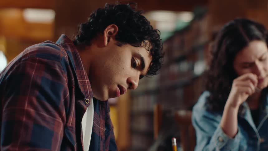 A young male student puts his phone away to focus on studying with others in the library