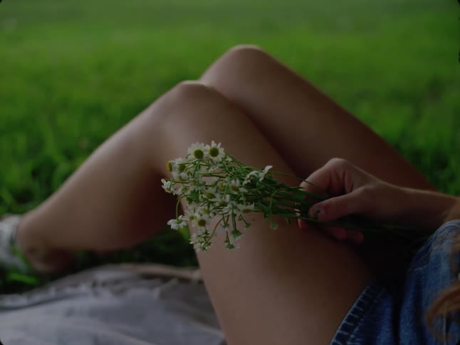 A young woman sitting on a blanket on a grass field holding flowers