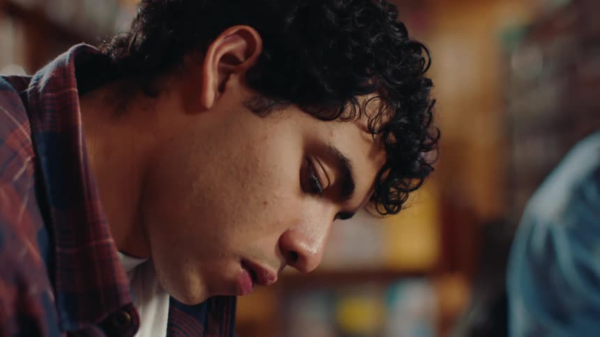 The face of a young man who is writing on a paper using a pencil and then he looks to the side