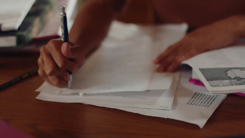A woman sitting at a desk writes on a sheet of paper with a pen