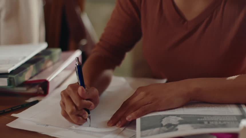 A woman writes on a piece of paper at a desk in a library