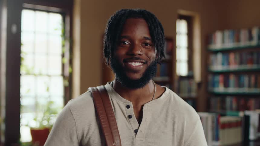 Portrait of young black male student in library smiling at camera