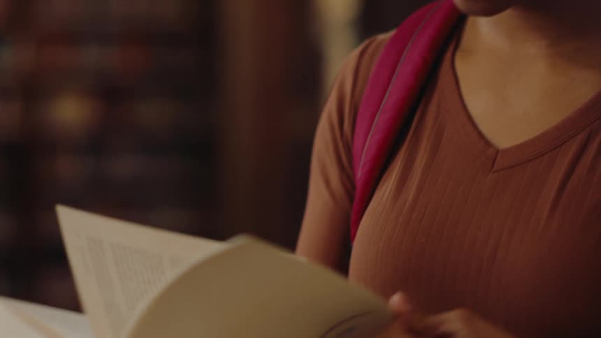 A young woman has a book in her hand and she is leafing through it while reading it