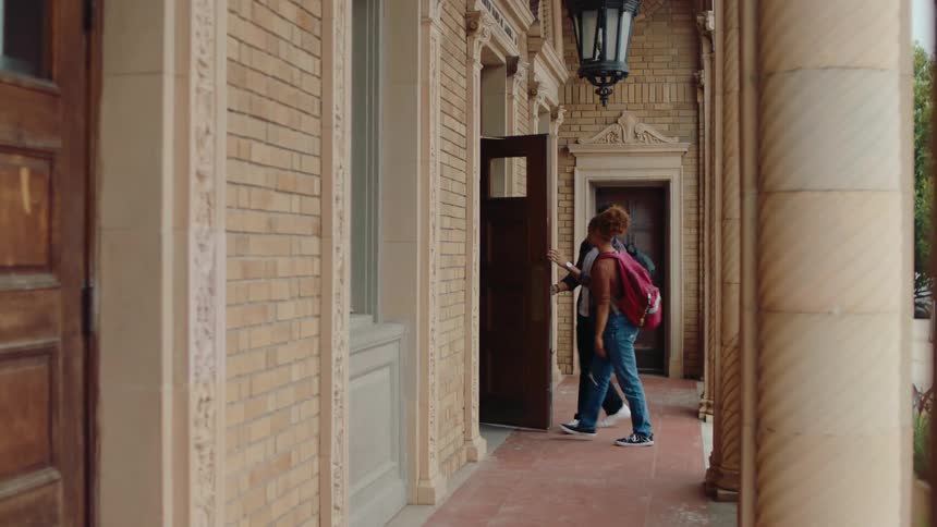 A guy and girl walk into a library building at a school
