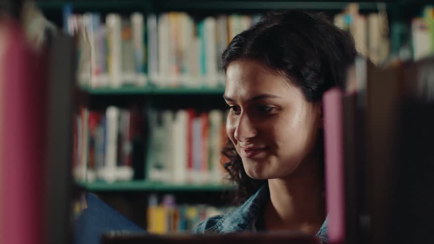 The face of a young woman who is looking at a bookshelf and then picks up one of them and leaves