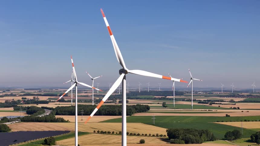 Aerial panorama of wind energy turbines moving across fields on a sunny day