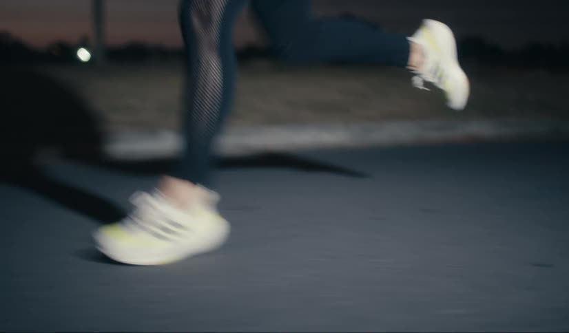 Feet of a person in white sneakers running on a road in a dark dawn