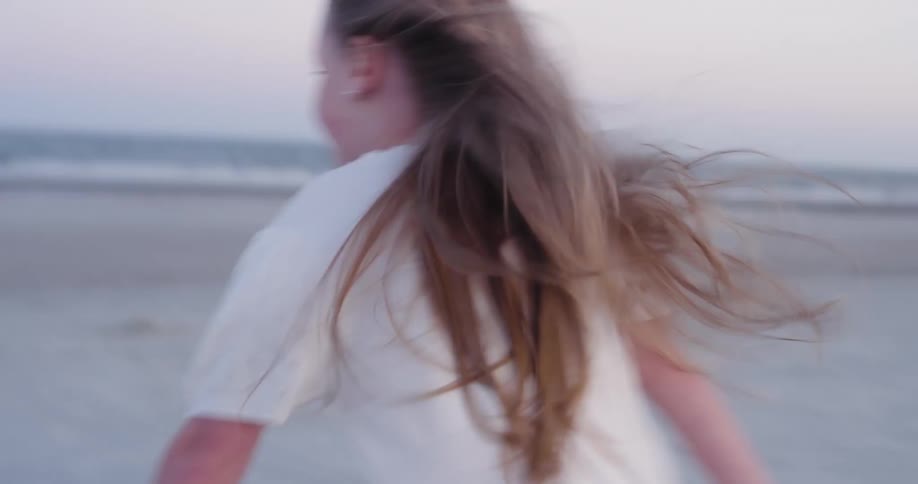 Little blonde girl running on the beach sand towards the sea