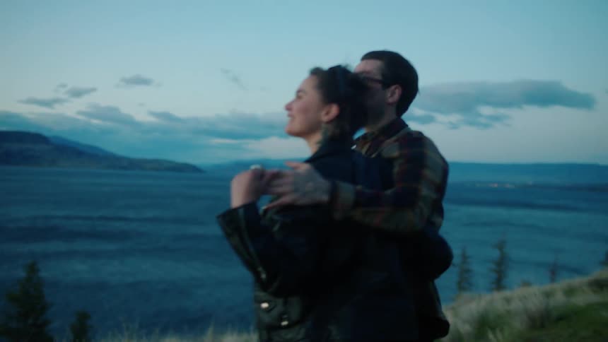 Man and woman holding hands hugging and kissing while standing in a lakeside setting