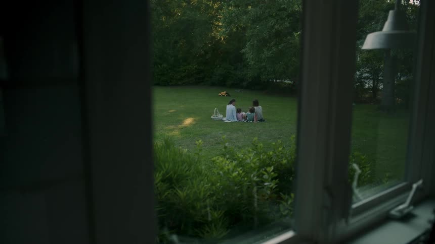 Two children and two women sitting in a garden on the grass in the backyard of a house