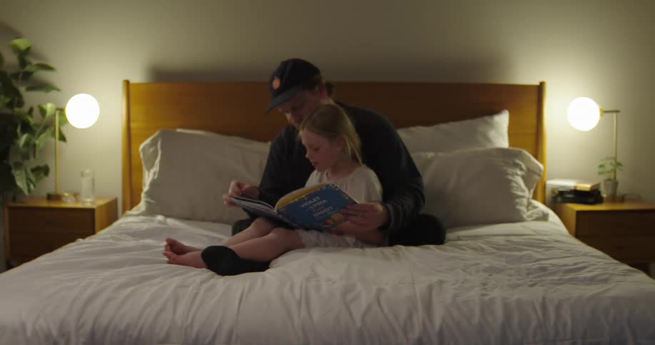 Father and daughter sitting together on the bed reading a book