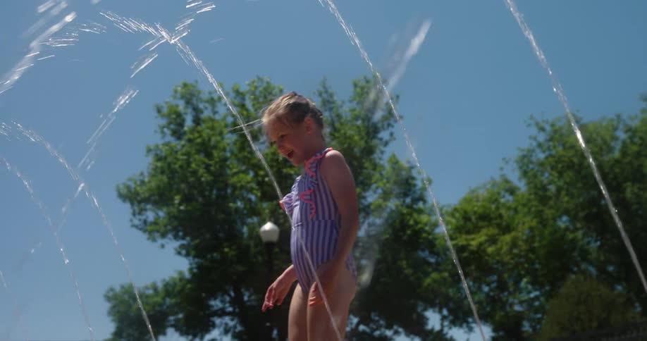 Little girl gets ready to run through a set of water sprinklers on a hot summer day