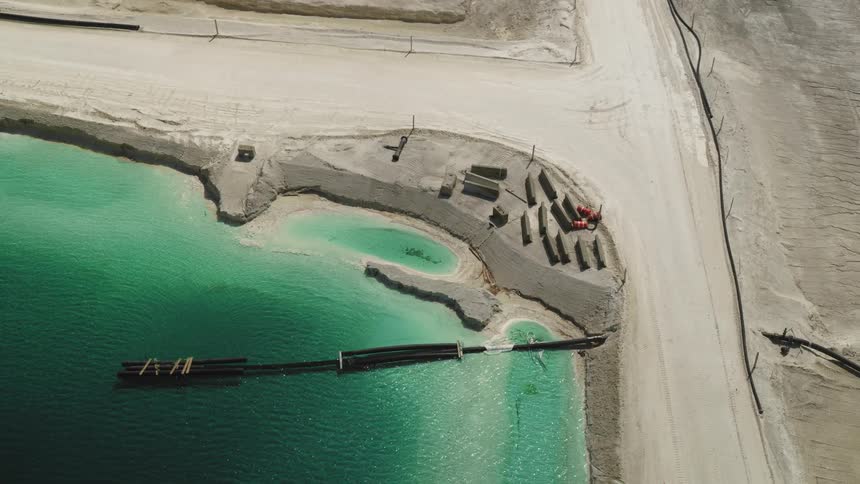 A bird flies past pipes in an industrial waste pond, aerial view