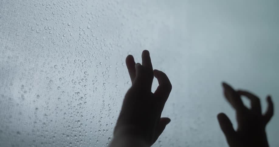 Young girl runs her fingers down window with raindrops on the outside