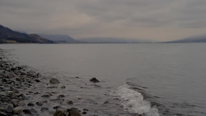 Waves roll into shore and over rocks along the coast with mountains in the distance
