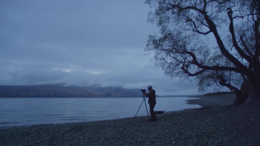 Male photographer with a camera and a tripod standing in front of a lake
