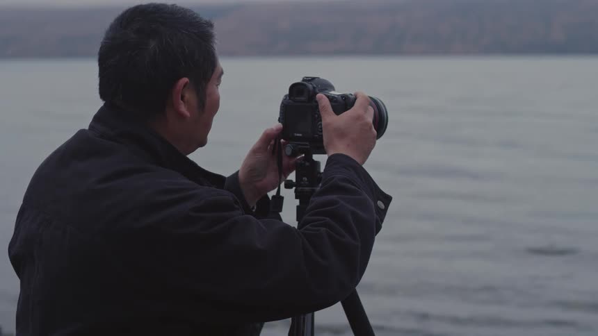 Man using a professional camera on a tripod in front of a lake