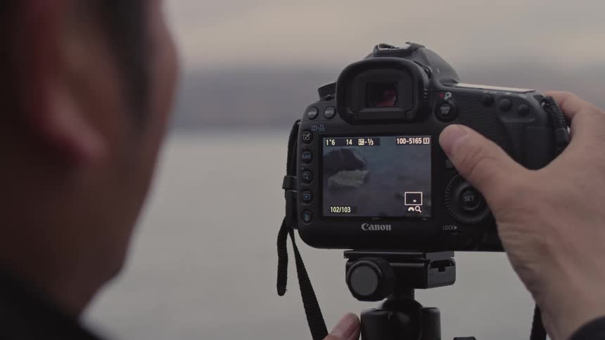 Male photographer adjusting a professional camera and zooming in on a landscape