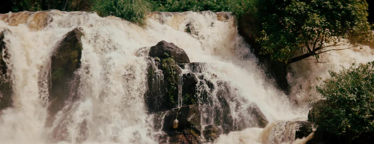 Muddy water foams while flowing down a waterfall near the woods