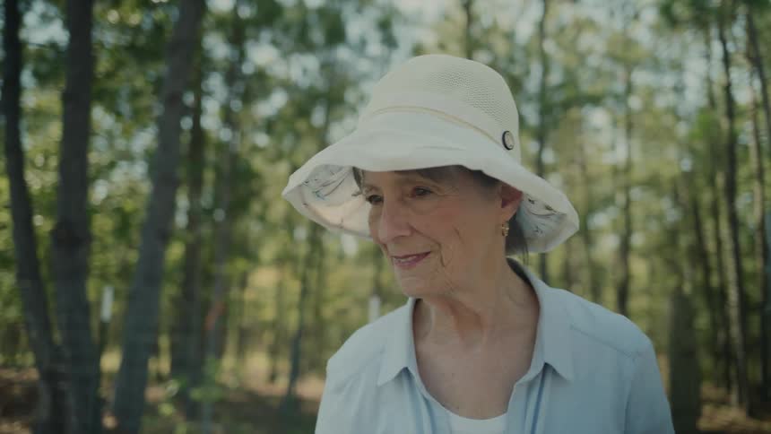 Older woman smiles while walking through the fenced area near the woods on a sunny summer day