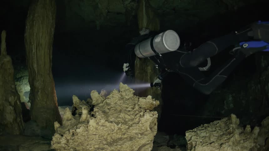 Diver blows bubbles and holds a flashlight while swimming into an underwater cavern