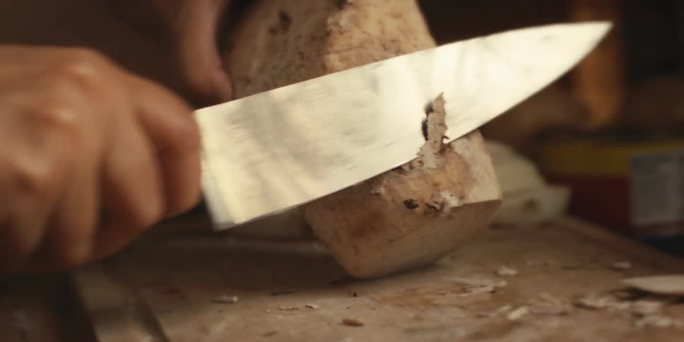 Hand holding a knife and removing the skin from a vegetable