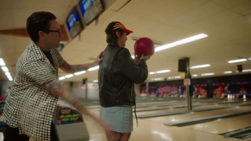 Man helping a woman throw a red bowling ball