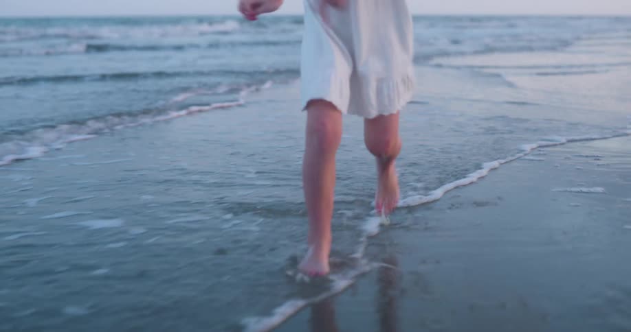 A white female in a white dress skips along a beach