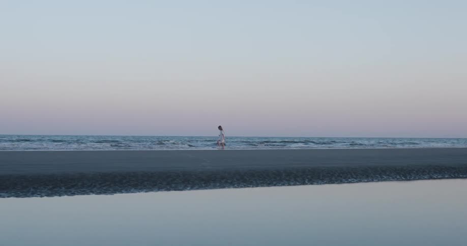 Young girl happily running on the shoreline at the beach in the distance at sunrise