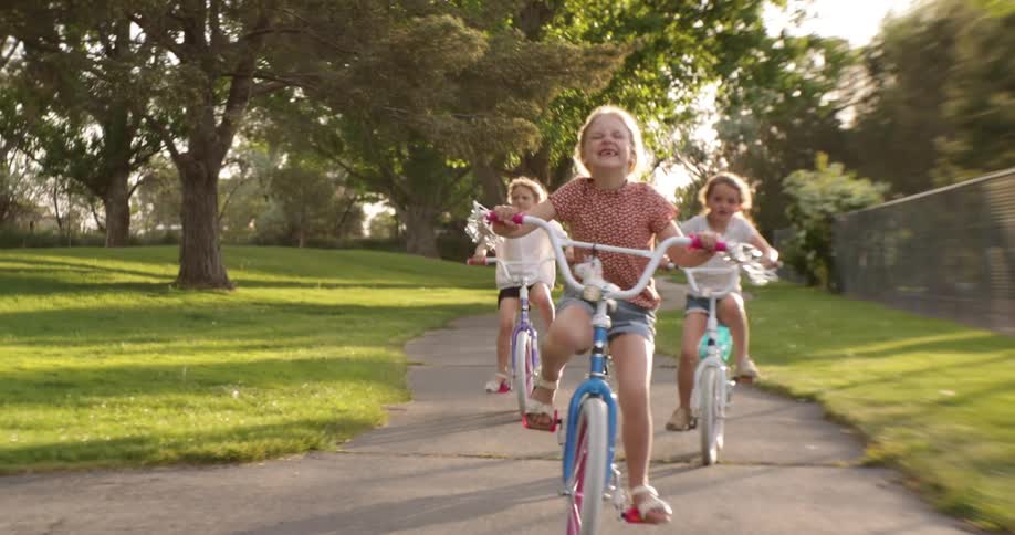 Girl laughing having fun riding her bike with friends on a pathway at a park