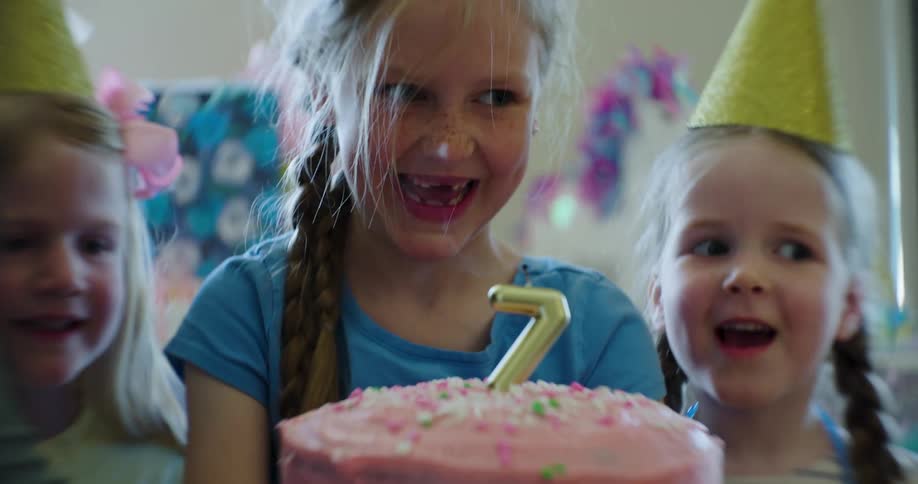 A young girls blows out a candle on a cake at her seventh birthday party with friends