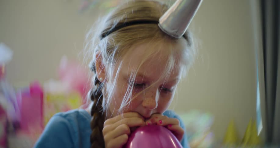 A young girl blows up a pink balloon for a party