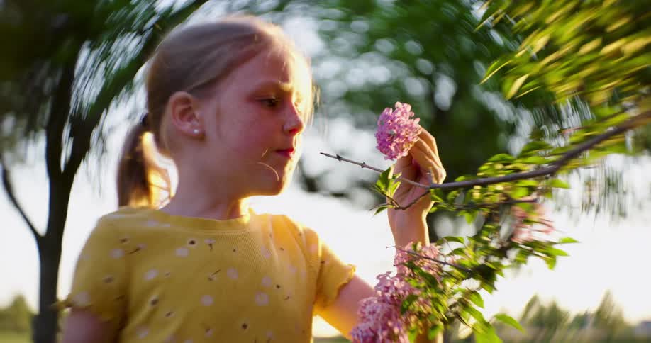 Little blonde girl picking a pink flower in a field